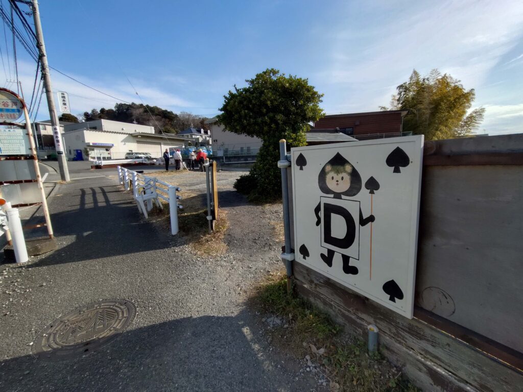 お地蔵様の祠に通じる小道がバス通りの歩道から枝分かれしている風景。「滝ヶ谷戸」バス停とトランプ兵が描かれた幼稚園の看板が目印。