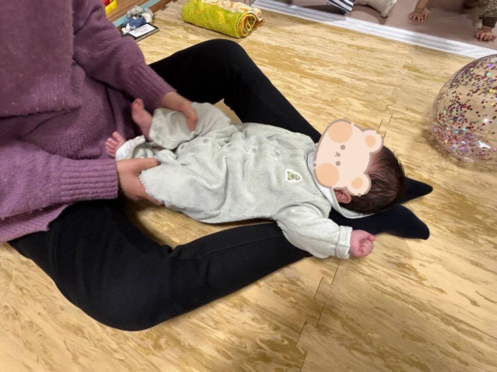 筆者の足の中に赤ちゃんを寝かせて、赤ちゃんの両足を持っています。