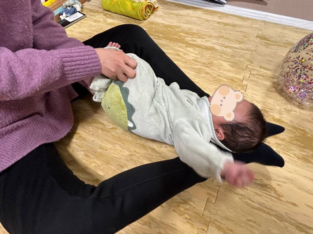 赤ちゃんの片足を持ち上げて反対側にねじっています。