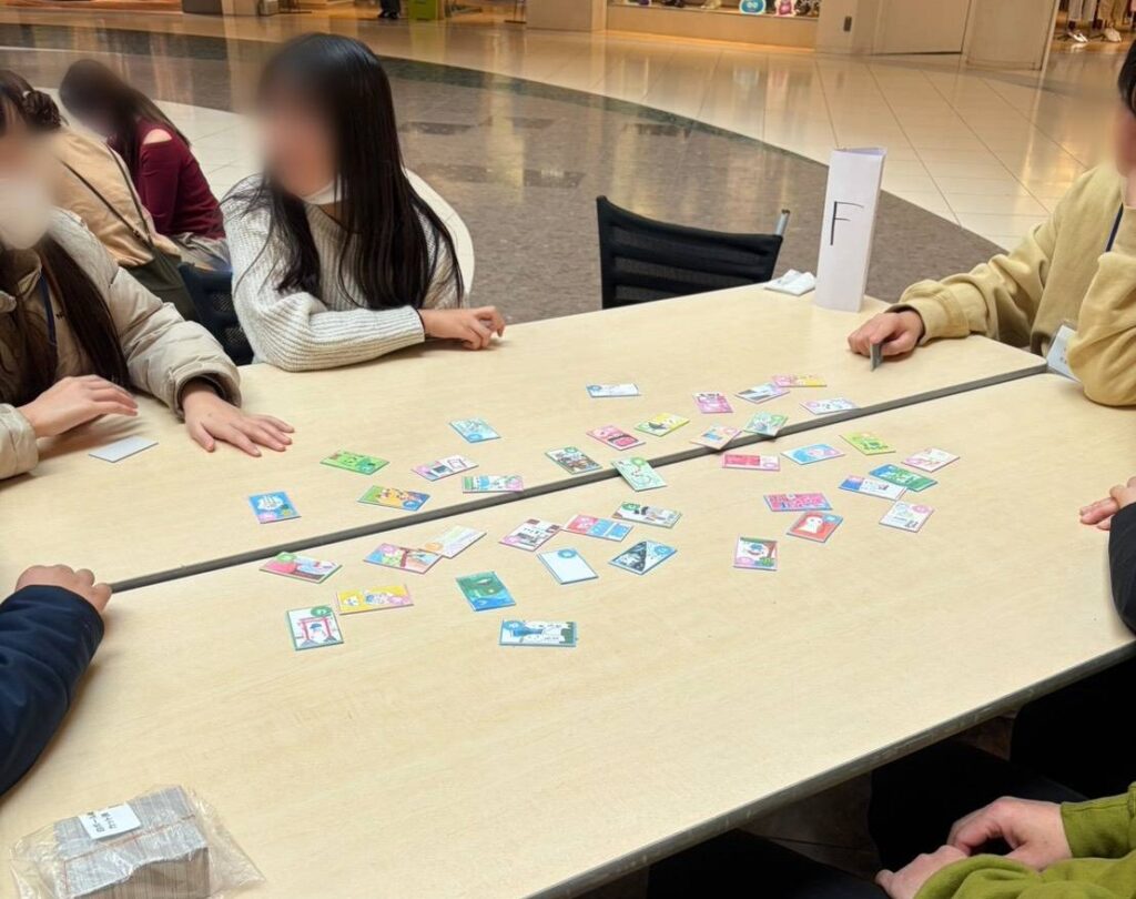 テーブルに並んだカルタを囲う参加者の人々